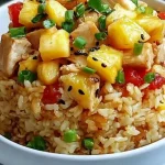 Bowl of fried rice topped with pineapple chunks, chicken, green onions, and black sesame seeds