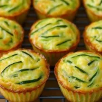Golden-baked zucchini egg cups cooling on a rack with visible zucchini strands